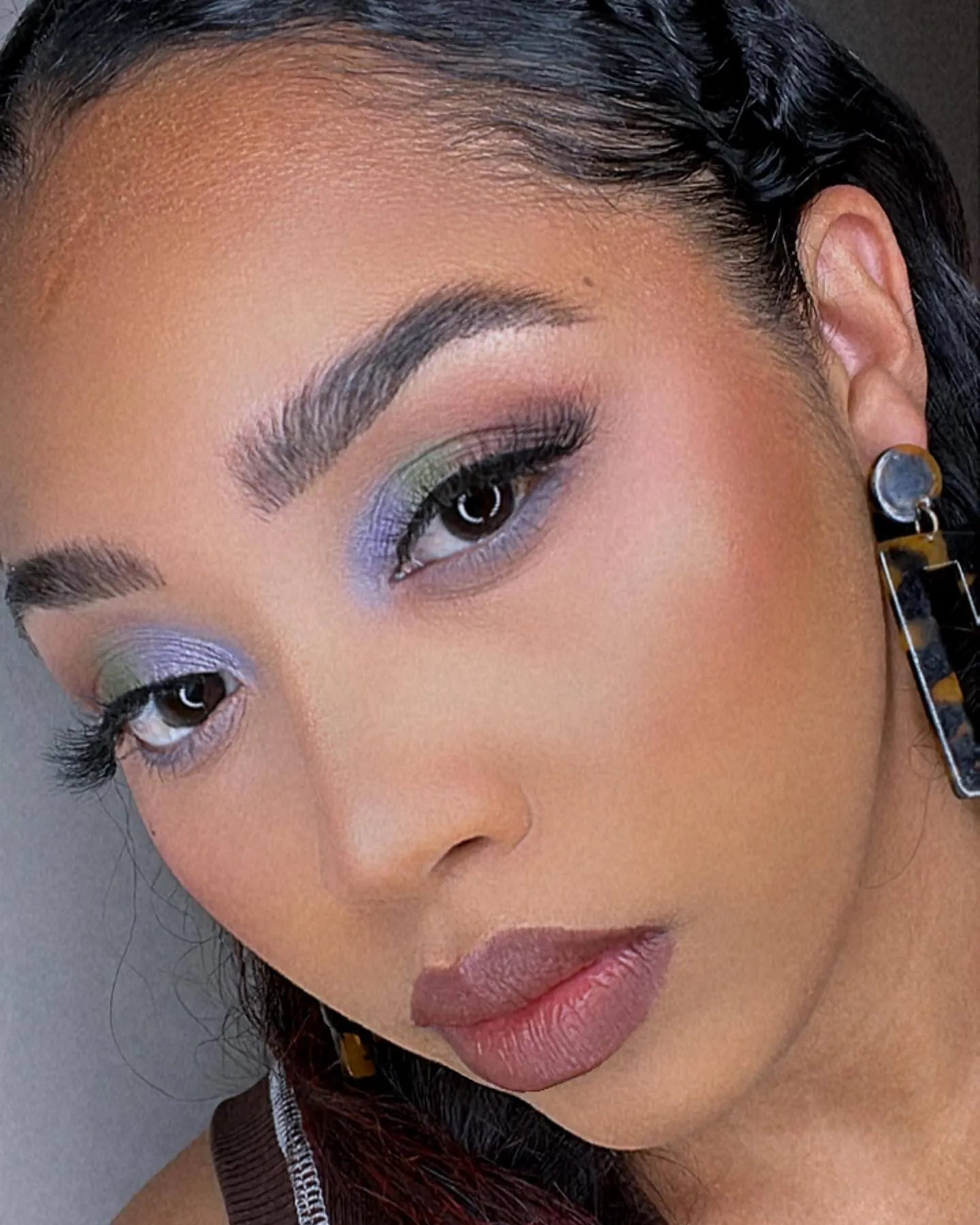 Close portrait with pastel blue and green eyeshadow, groomed brows, and a muted lip.